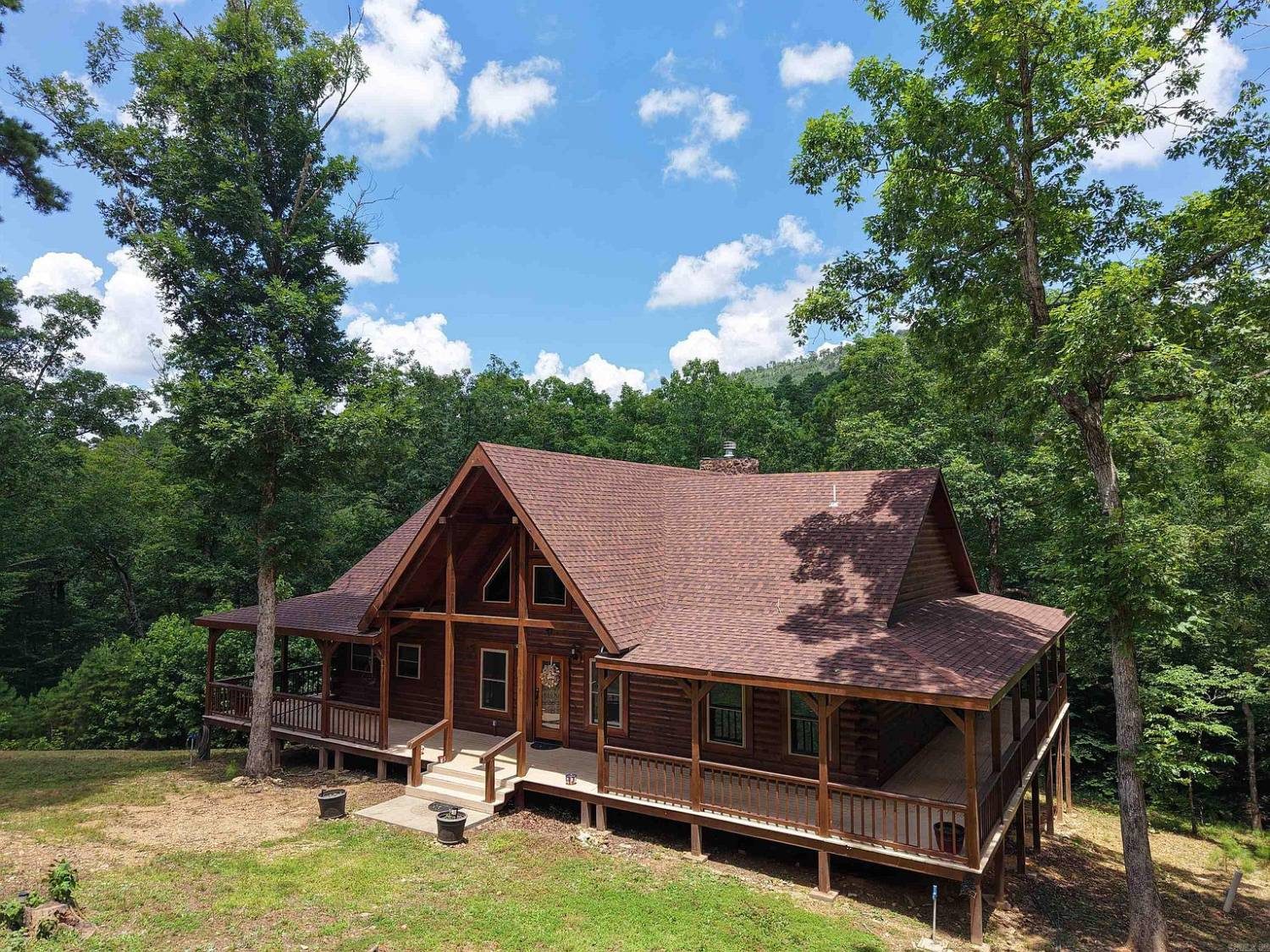 Creekside Cabin, a 2022 custom log home with wraparound porches under the oaks